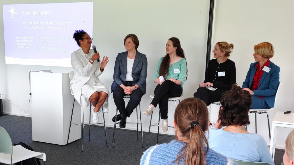 Fünf Frauen sitzen in einem hellen, weißen Raum auf Hochstühlen und diskutieren miteinander über über das Berufsbild Infektionsforscherin und entscheidende Faktoren auf dem Karriereweg als Wissenschaftlerin. Die Frau ganz links hält das Mikrofon und lacht. Von links nach rechts sind die Frauen Marlylyn Addo, Ulrike Protzer, Alexandra Simons, Sandra Ciesek und Ute Habel. Foto: René Lesnik