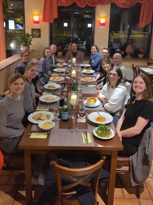 Die Mentees und Mentor:innen des ACHIEVE Mentoring Meetings sitzen beim Abendessen im italienischen Restaurant zusammen an einem gedeckten Tisch.